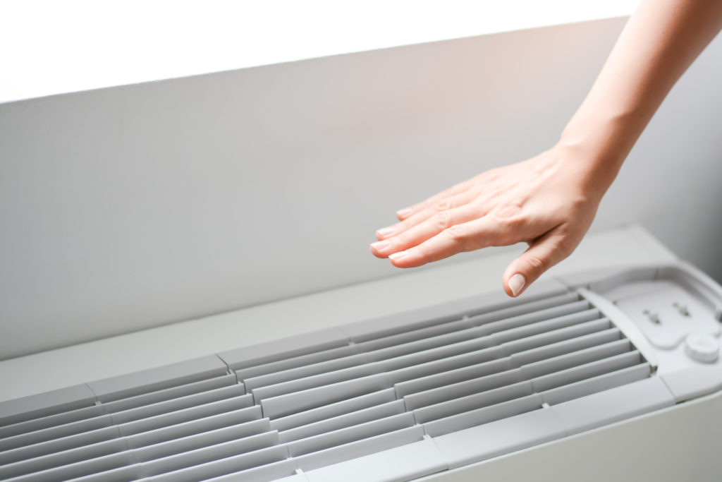 Focused view on a hand hovering above a ductless heating system, feeling the temperature.