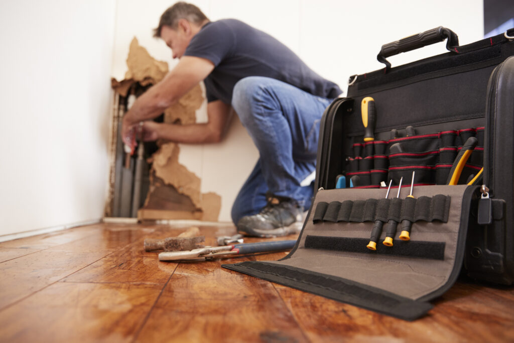 Plumber repairing a burst pipe in a wall. Open tool bag in foreground.